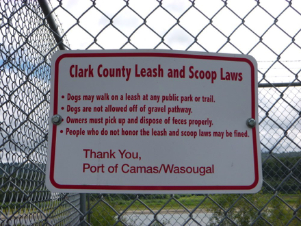 Sign on Columbia River Dike Trail – dogs may walk on leash on the gravel pathway – pick up and dispose of feces Sign on Columbia River Dike Trail – dogs may walk on leash on the gravel pathway – pick up and dispose of feces